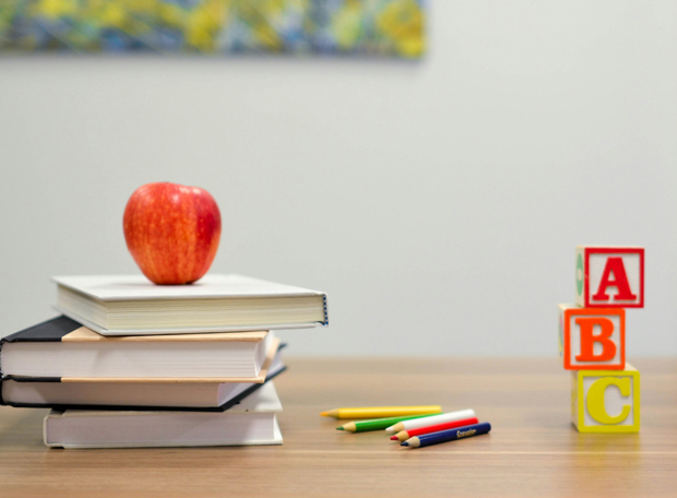 Stapel Bücher mit Apfel, Buntstiften und ABC-Bausteinen auf einem Tisch