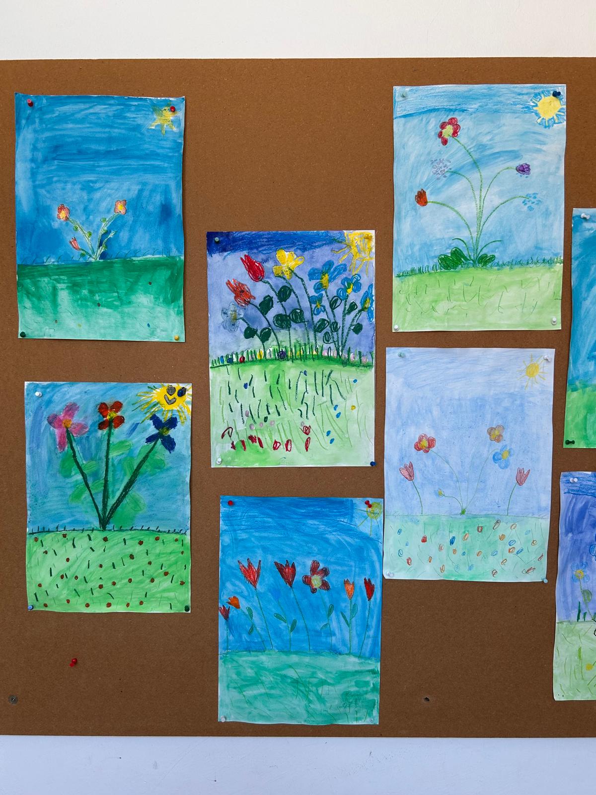 Kinderzeichnungen von Blumen auf einer Pinnwand, mit unterschiedlichen Blütenformen, leuchtenden Farben und sonnigen Himmelsszenen.